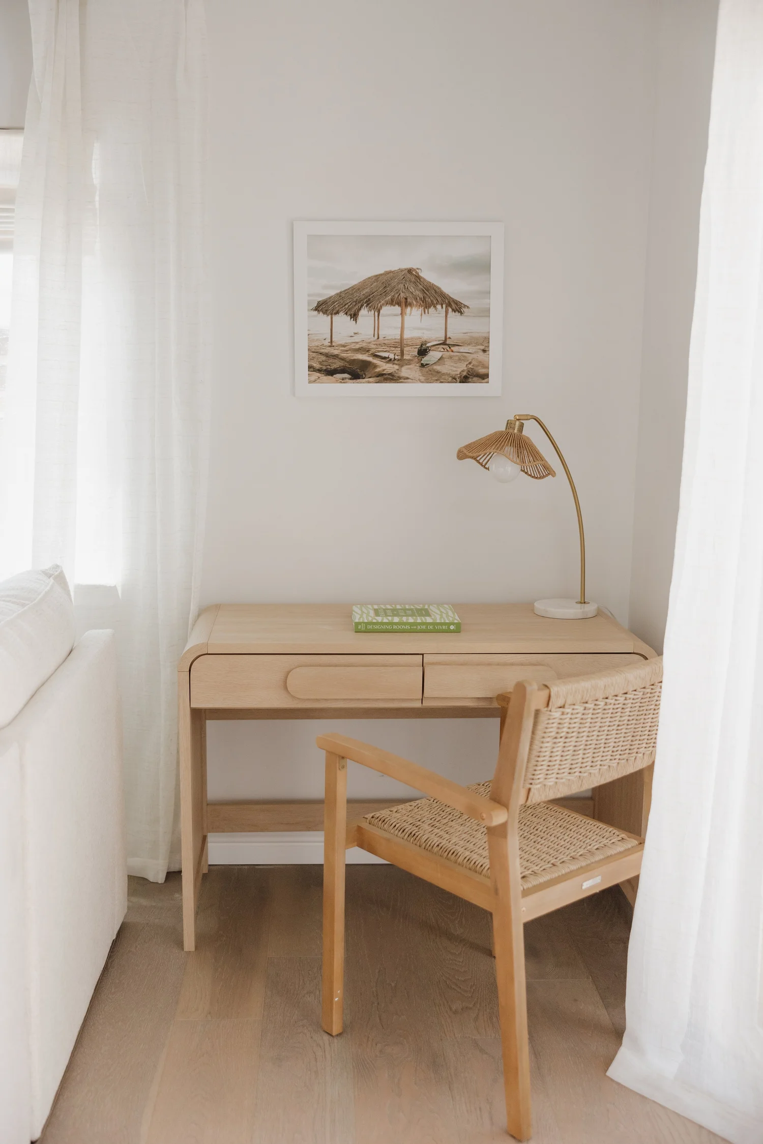 Writing desk with a rattan chair and beach art by the window at Coastal Palm in Pacific Beach, designed by Salt and Sky Lodging Co.