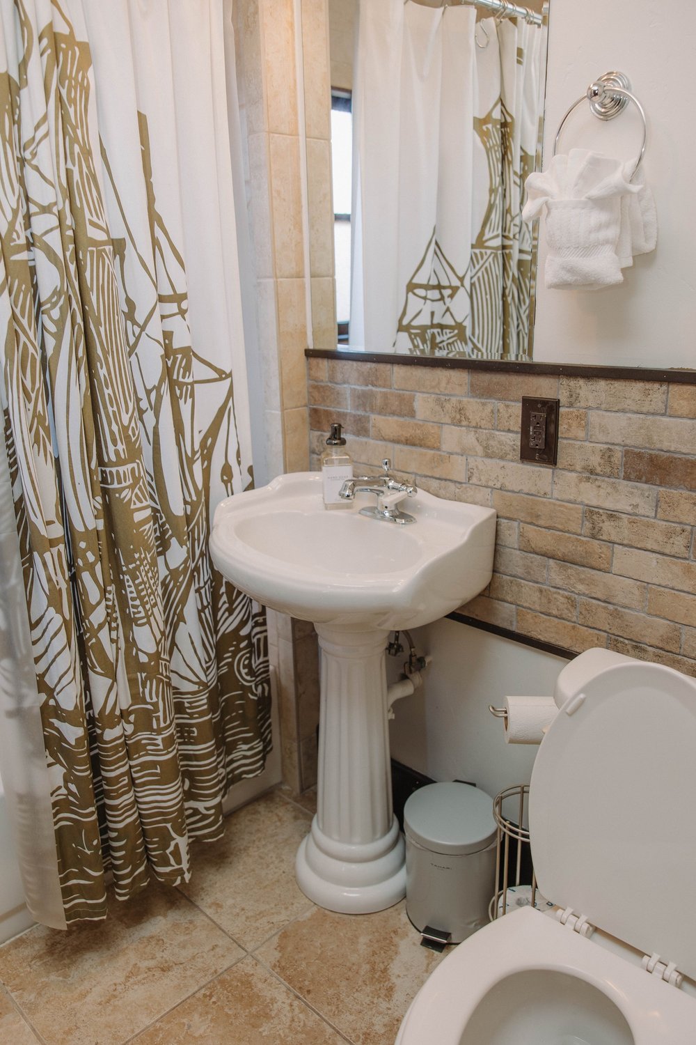 A first floor bathroom at Palm Parkside with a pedestal sink, a brick tile backsplash and a sailing ship shower curtain