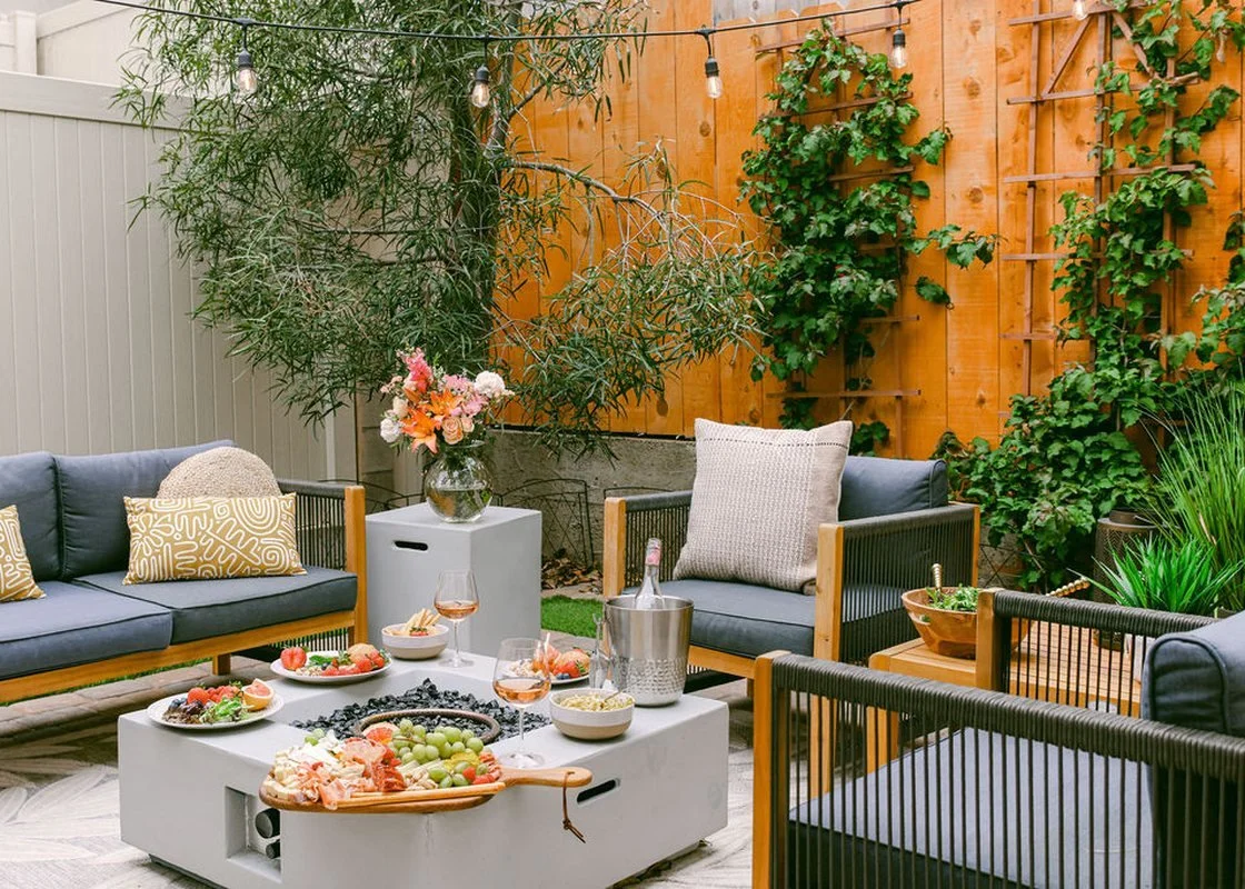 The fenced back patio at OB Surfer's Paradise in Ocean Beach, with a gas fire table, lounge seating and string lights