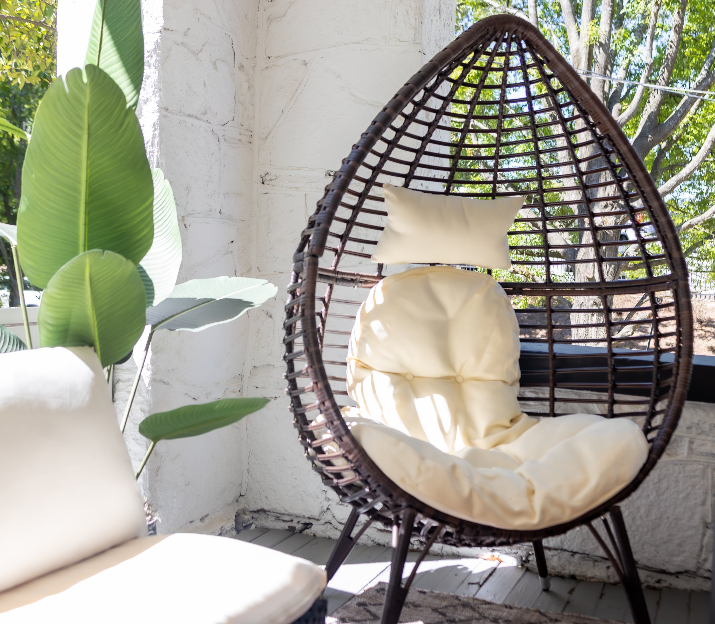 Wicker egg chair with cream cushions on the porch at Elmsgate in Birmingham, designed by Salt and Sky Lodging Co.