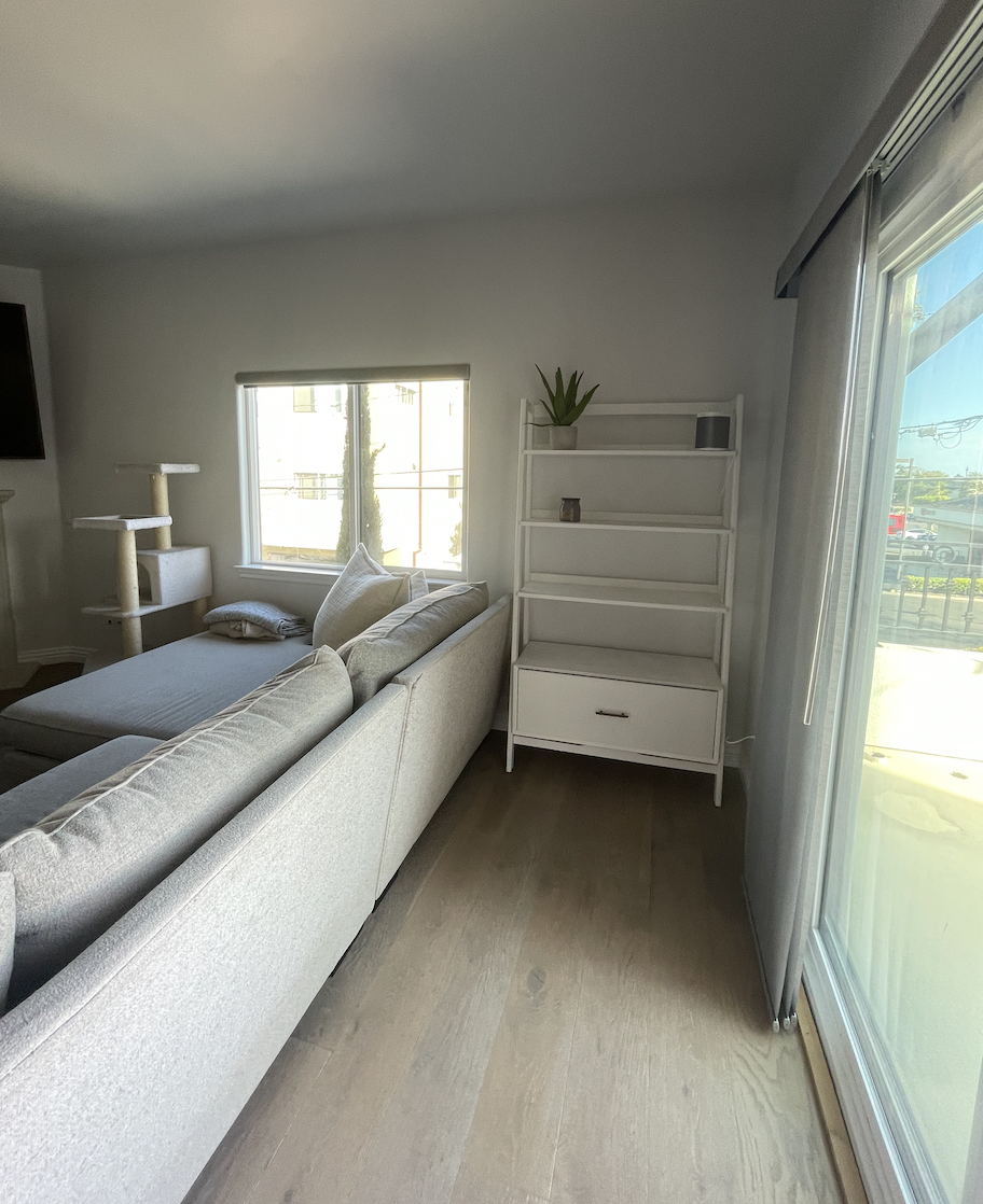 Before: Living room with a sectional and a bookshelf at Coastal Palm in Pacific Beach