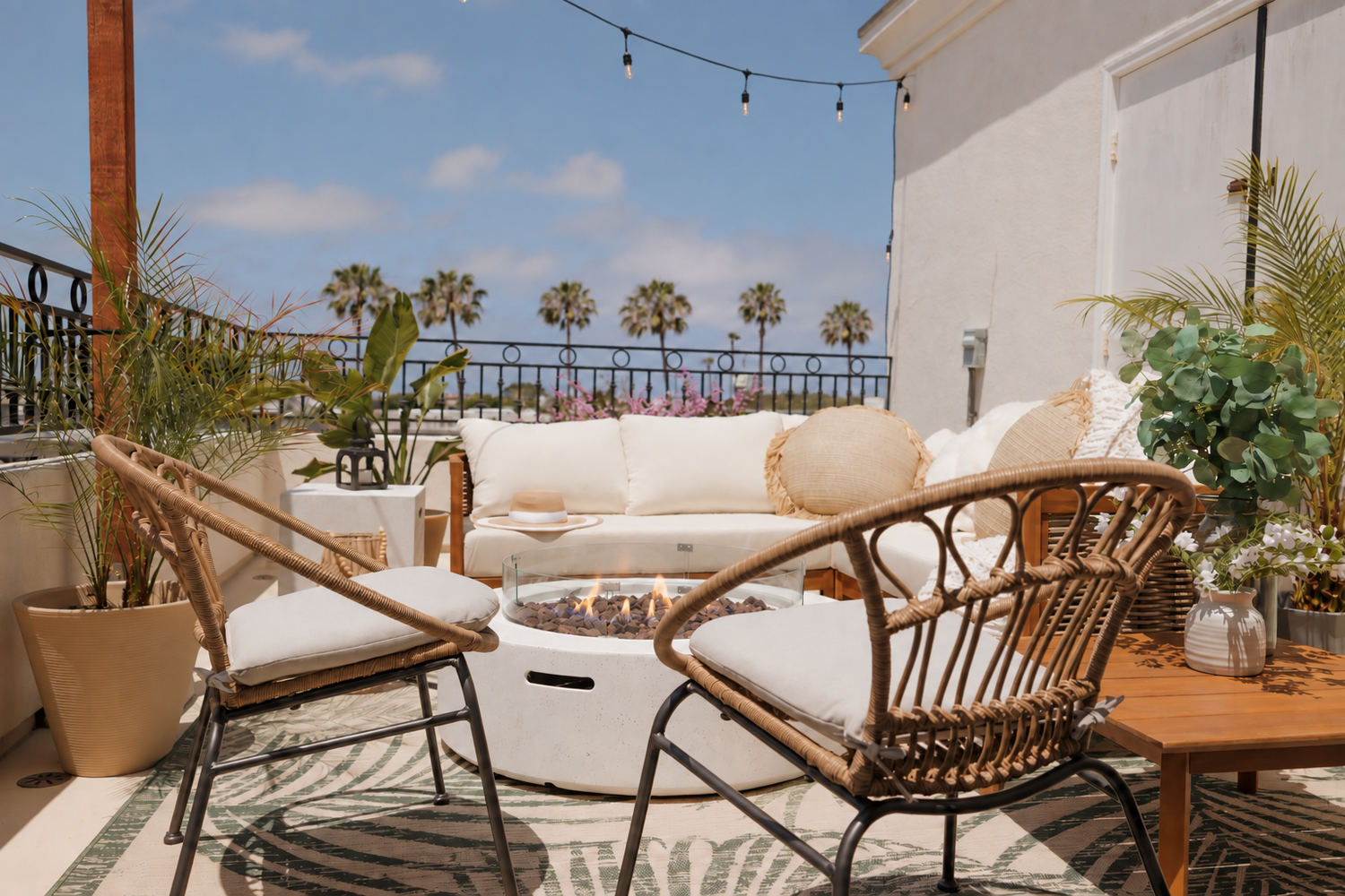 A sunny rooftop patio at our Pacific Beach rental, with wicker chairs around a fire pit and palm trees beyond