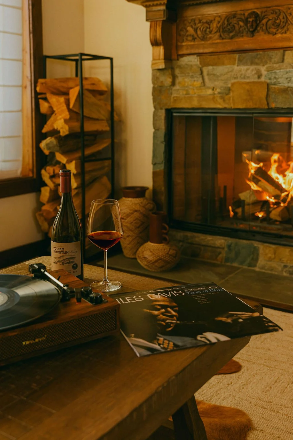 Stone fireplace with a lit fire and wine on the coffee table