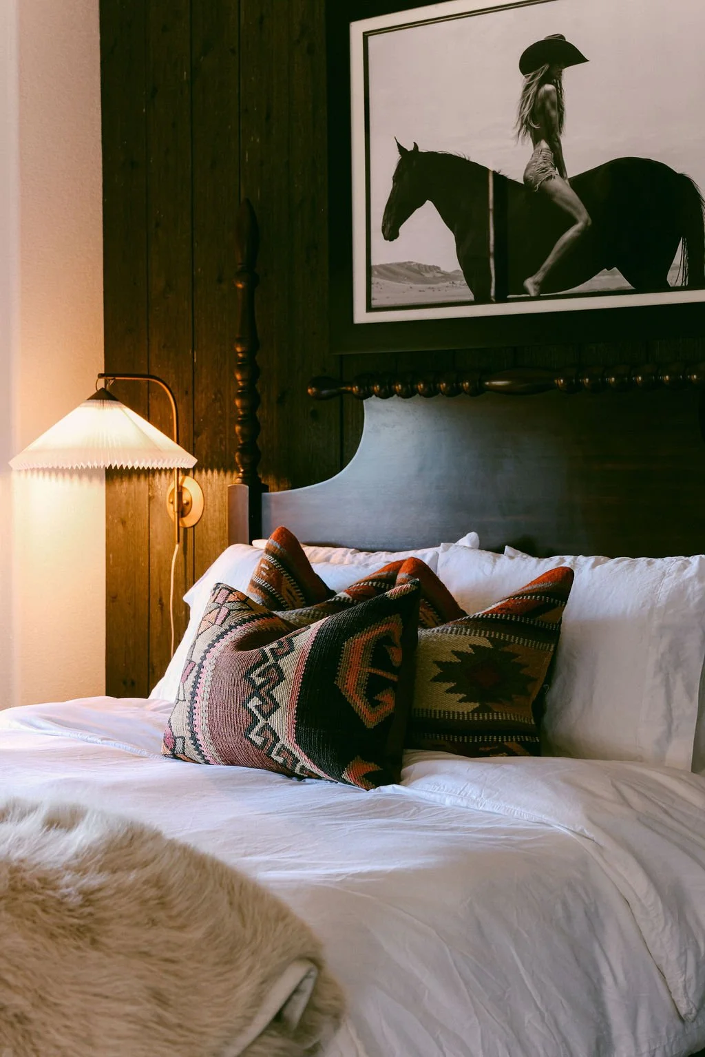 Bedroom with a black upholstered bed, western throw pillows and framed horse and rider art