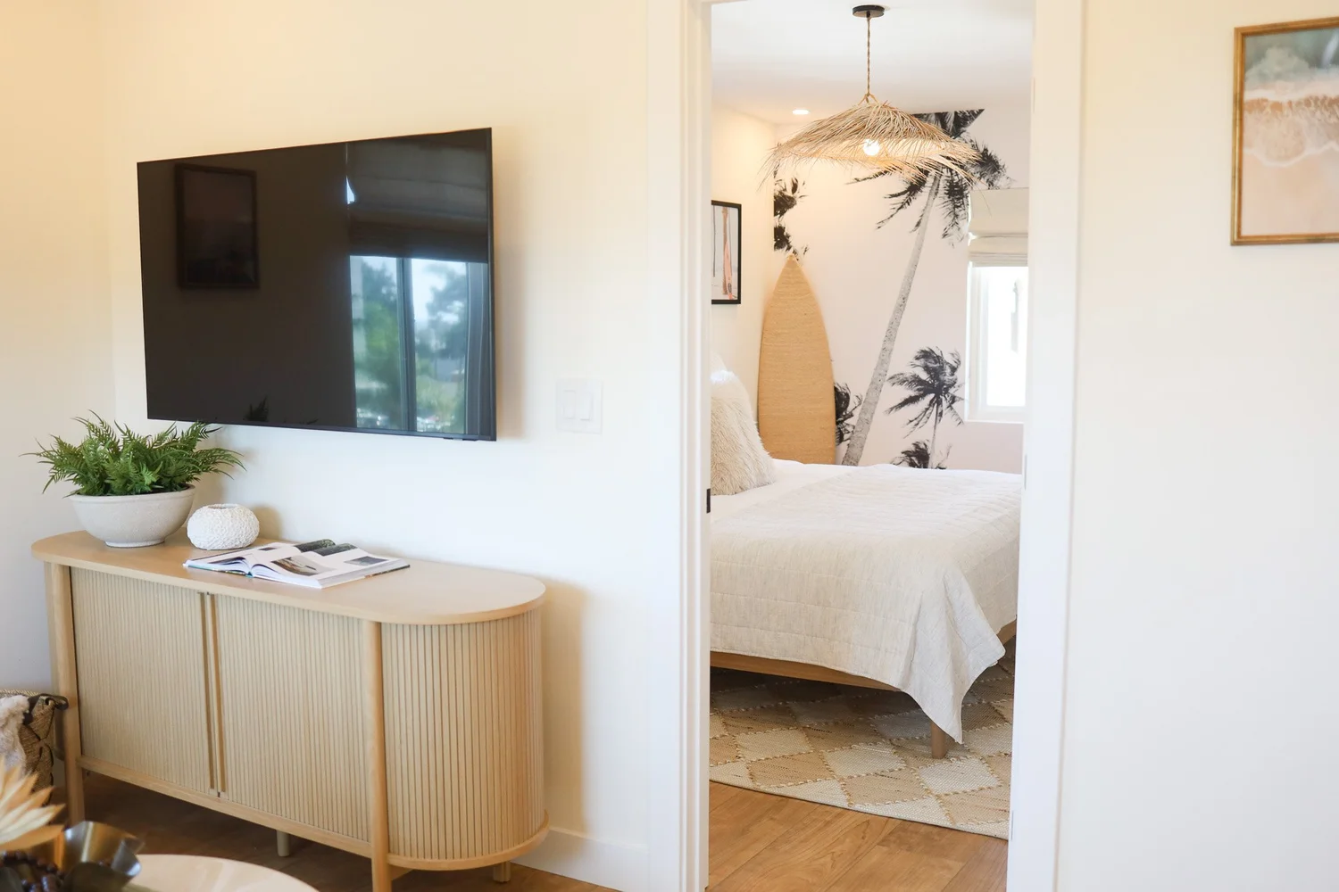 Living room with a curved wood console and a view into the bedroom at Clementine C in Oceanside, designed by Salt and Sky Lodging Co.