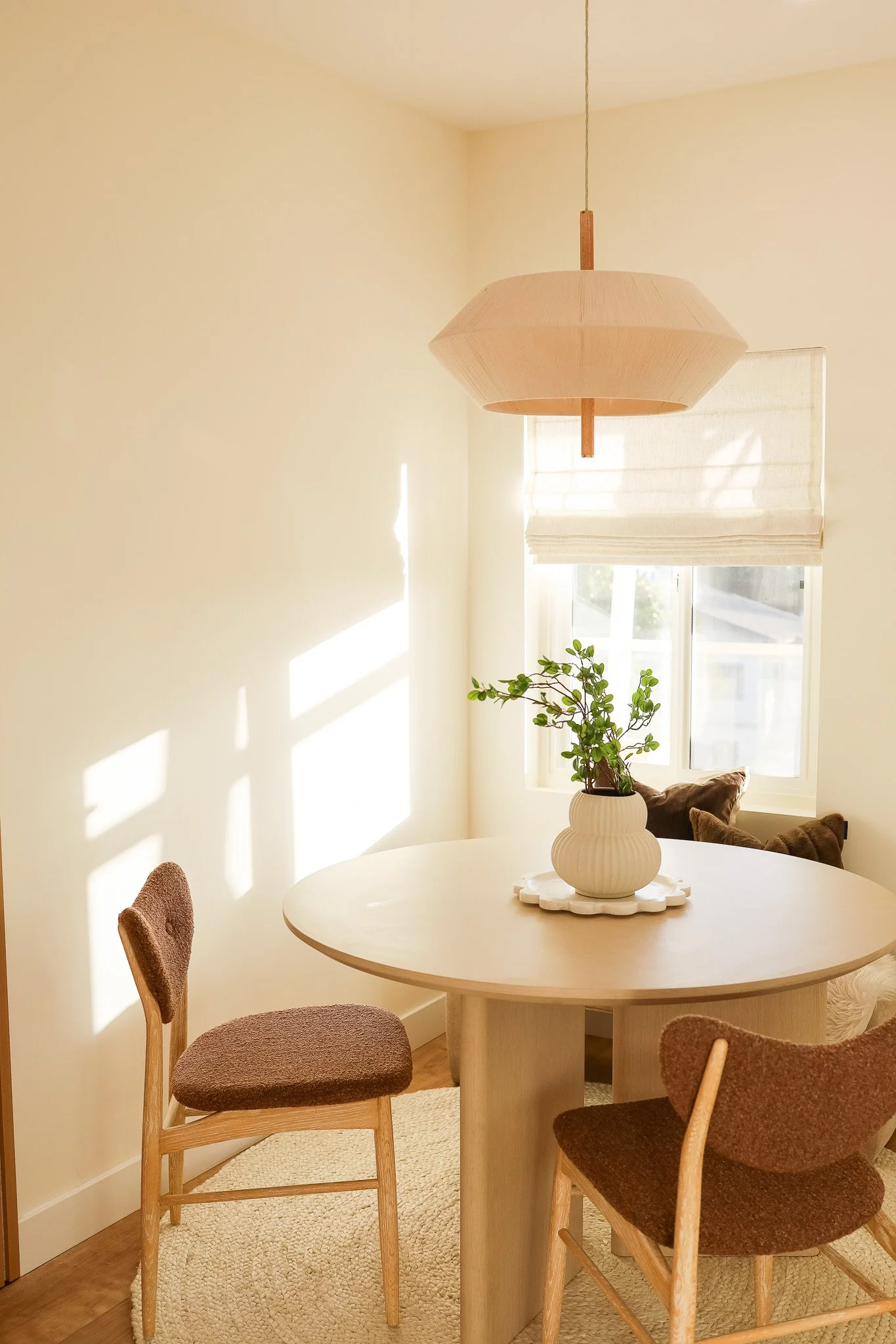 A sunlit dining nook at The Swell in Oceanside, renovated and designed by Salt & Sky, with a round table, woven chairs and a paper pendant