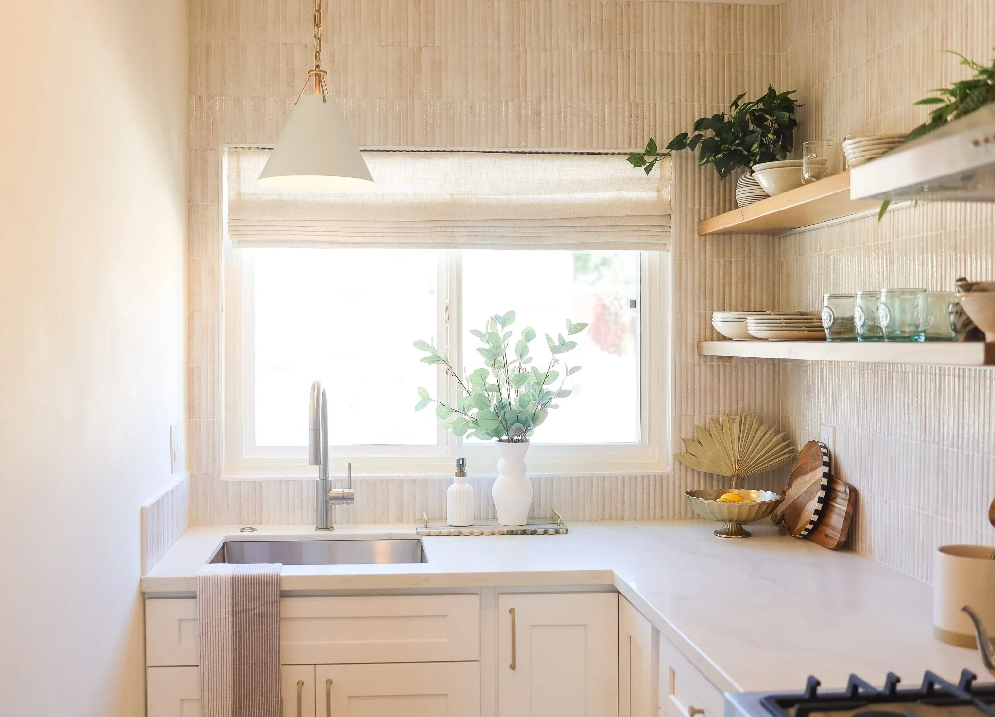 Kitchen with floating shelves, a white sink and a window at Clementine C in Oceanside, designed by Salt and Sky Lodging Co.
