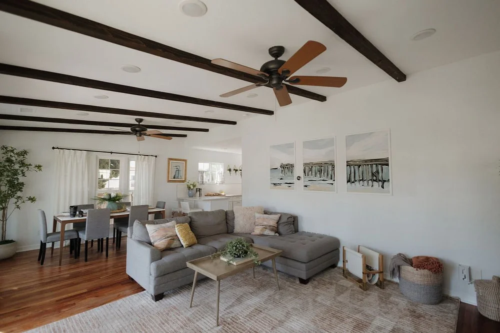 The open living and dining room in The Villa with wood beams, ceiling fans and a gray sectional