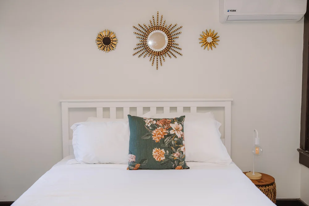 A queen bed with a green floral pillow and gold sunburst mirrors in a first floor bedroom at Palm Parkside