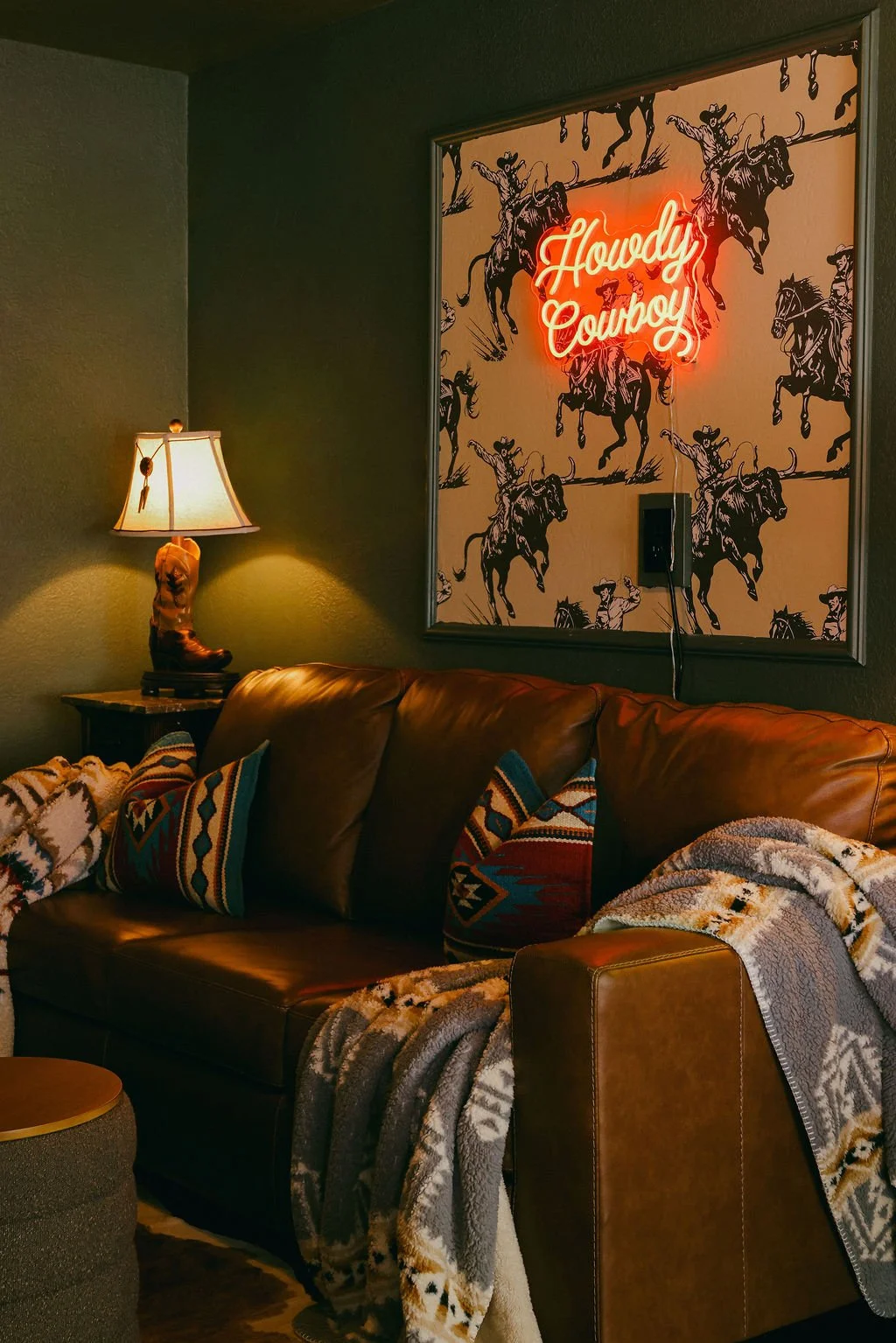 Den with a leather sofa, western art and a neon sign on a dark green wall