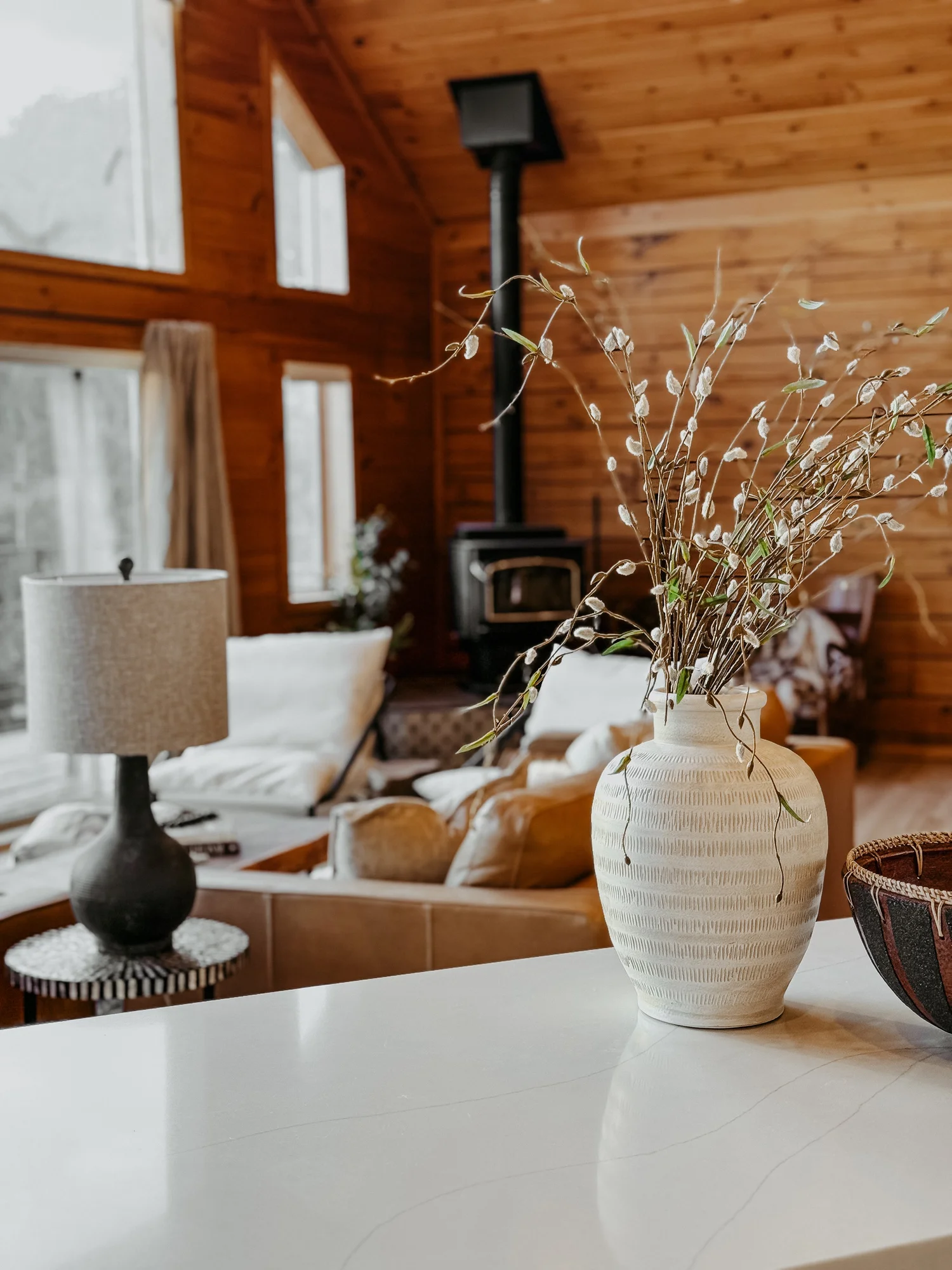 Living room with a wood stove, white sofas and a vase of branches at Dark Moon Chalet in Julian, designed by Salt and Sky Lodging Co.