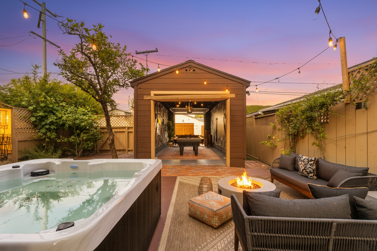 The backyard at Palm Parkside at dusk, with the hot tub, outdoor sofas, string lights and the lit garage game room