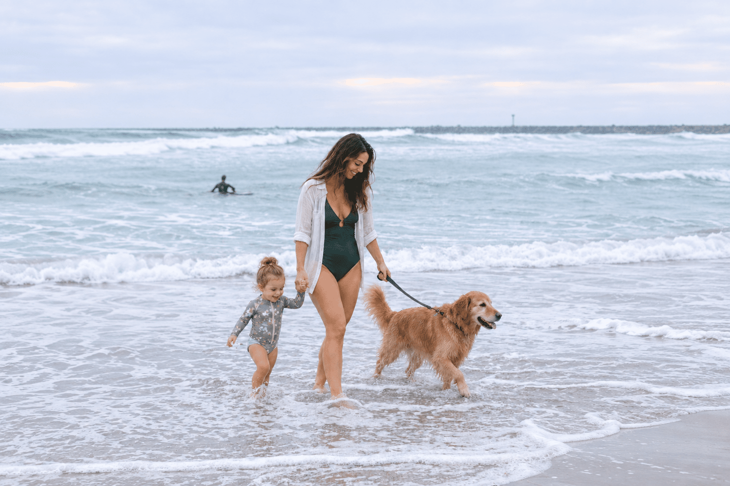 A mother, her young daughter and their golden retriever walking through the surf at Ocean Beach, San Diego