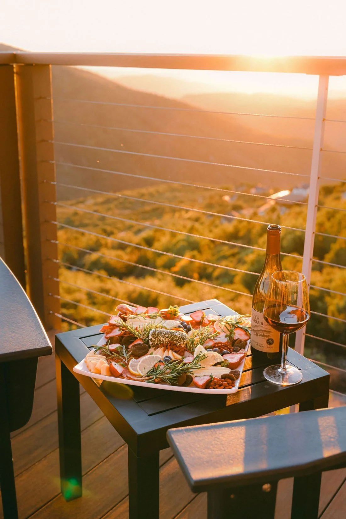 A charcuterie board and a bottle of wine on the deck table as the sun goes down over the Julian hills