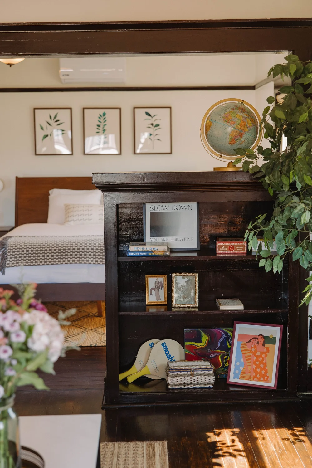 The upstairs master suite at Palm Parkside, with the king bed behind a dark wood bookshelf, a globe and botanical prints