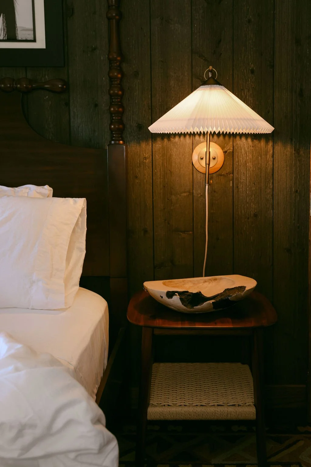 Bedside table with a pleated wall sconce against dark wood paneling