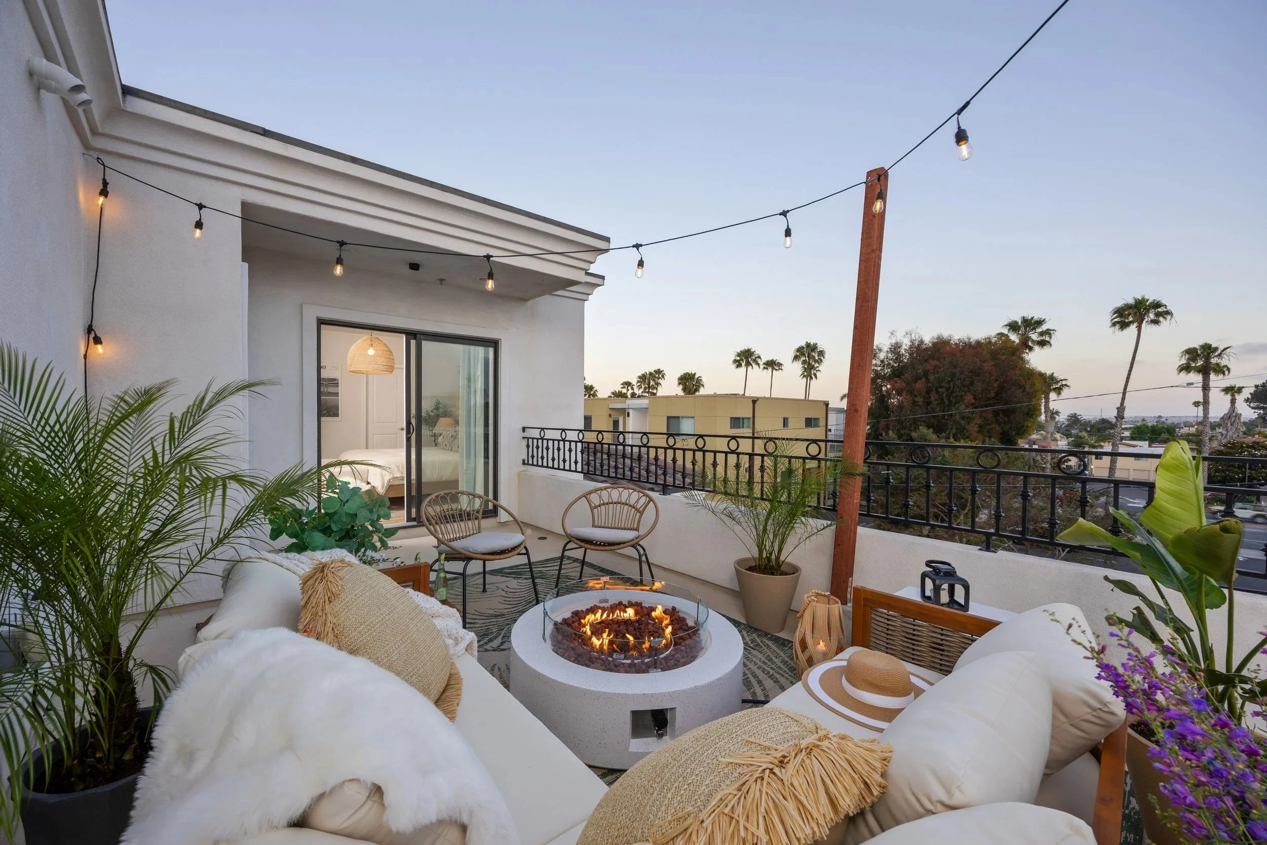 Rooftop balcony at Coastal Palm, a Pacific Beach vacation rental, with a firepit, string lights, and palm tree views at dusk