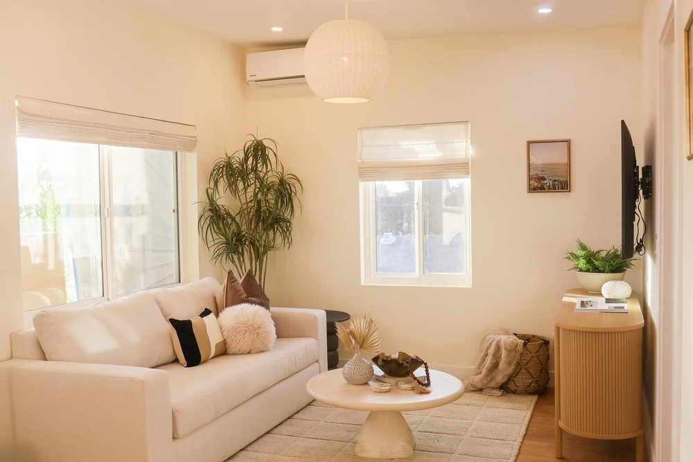The living room with a cream sofa, a round coffee table and bright windows in Unit Three at The Swell, Oceanside