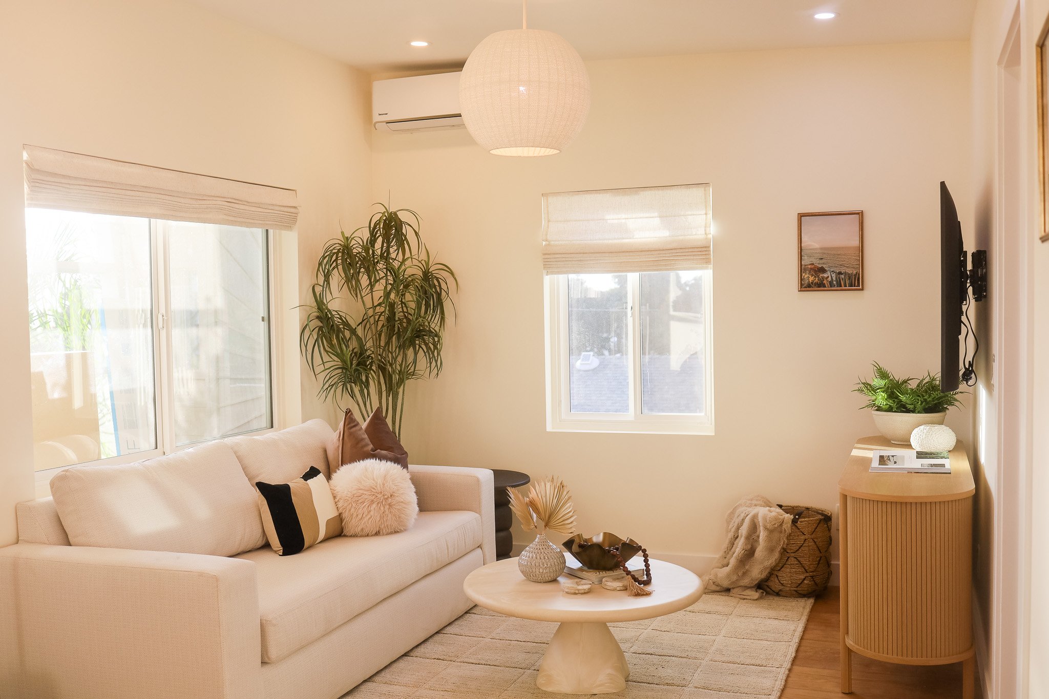 The living room with a cream sofa, a round coffee table and bright windows in Unit Three at The Swell, a monthly rental in Oceanside