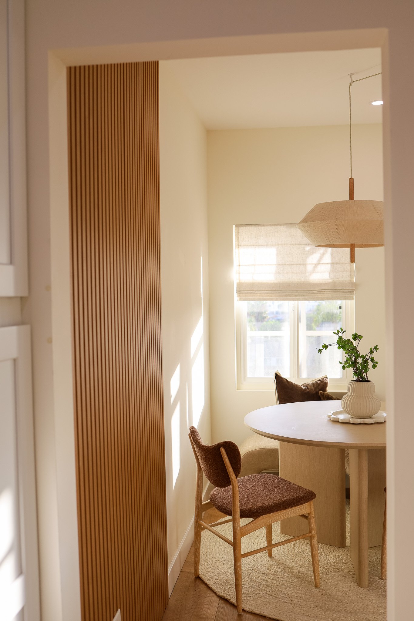 A sunny dining nook at The Swell in Oceanside, with a slatted wood wall, a round table, a leather chair and a paper pendant light