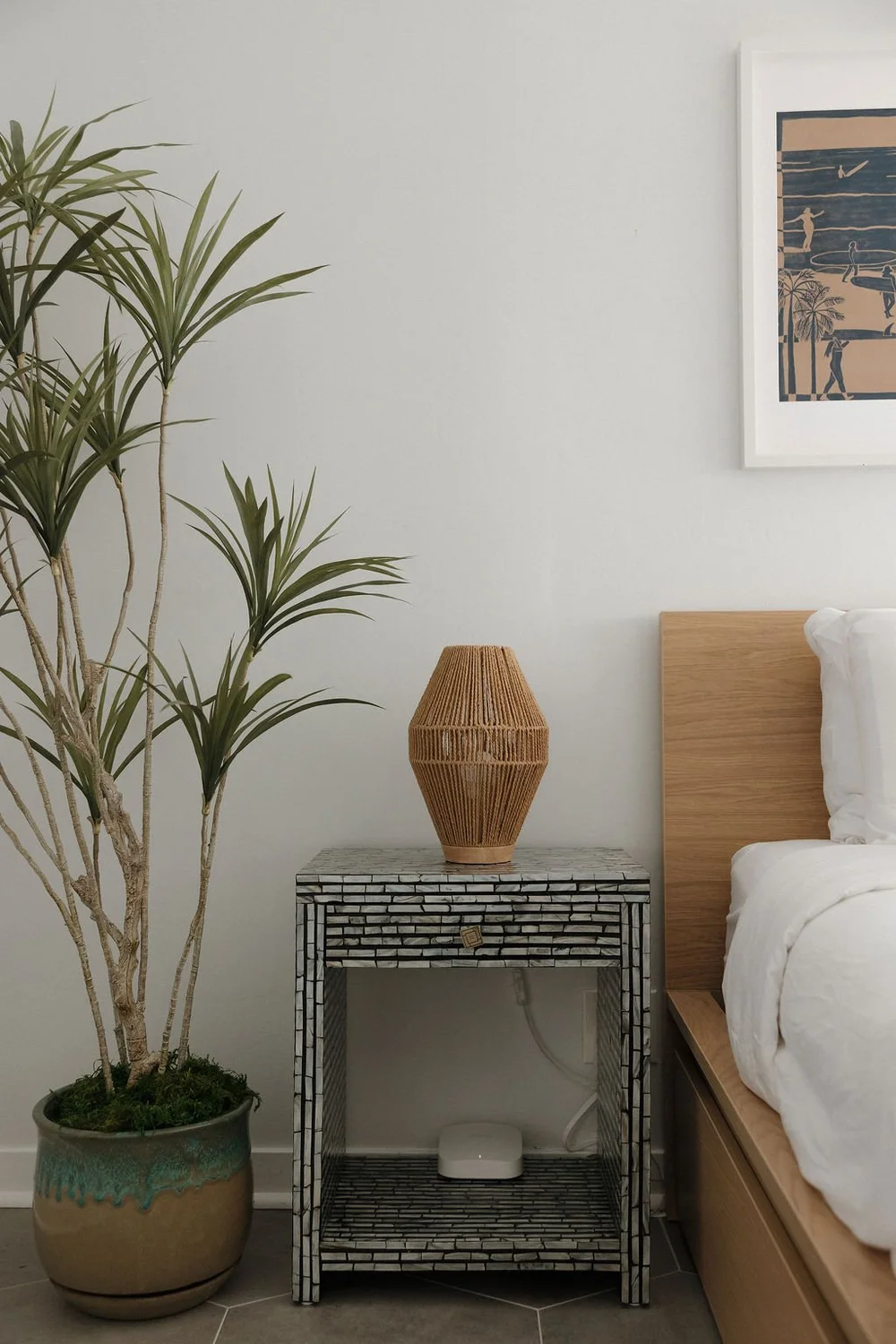 A bedroom in The Villa with a woven lamp, a palm and beach art