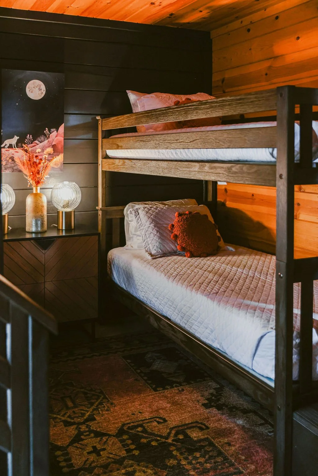 Bunk room with wood bunk beds, pink bedding and a vintage rug at Dark Moon Chalet in Julian, designed by Salt and Sky Lodging Co.