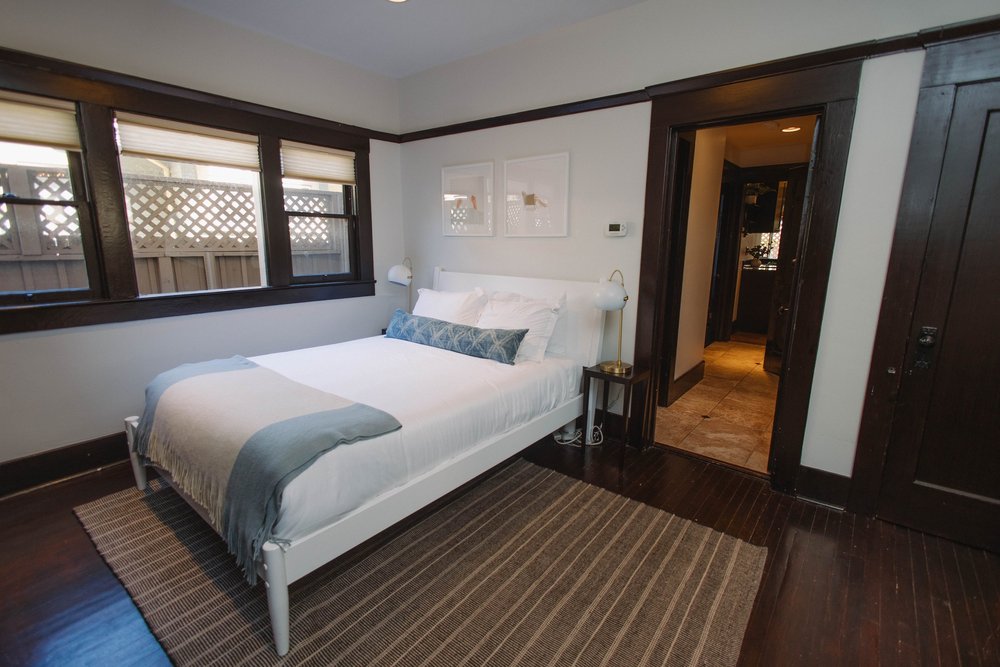 A queen bedroom on the first floor at Palm Parkside, with a white bed, a woven rug and dark wood trim