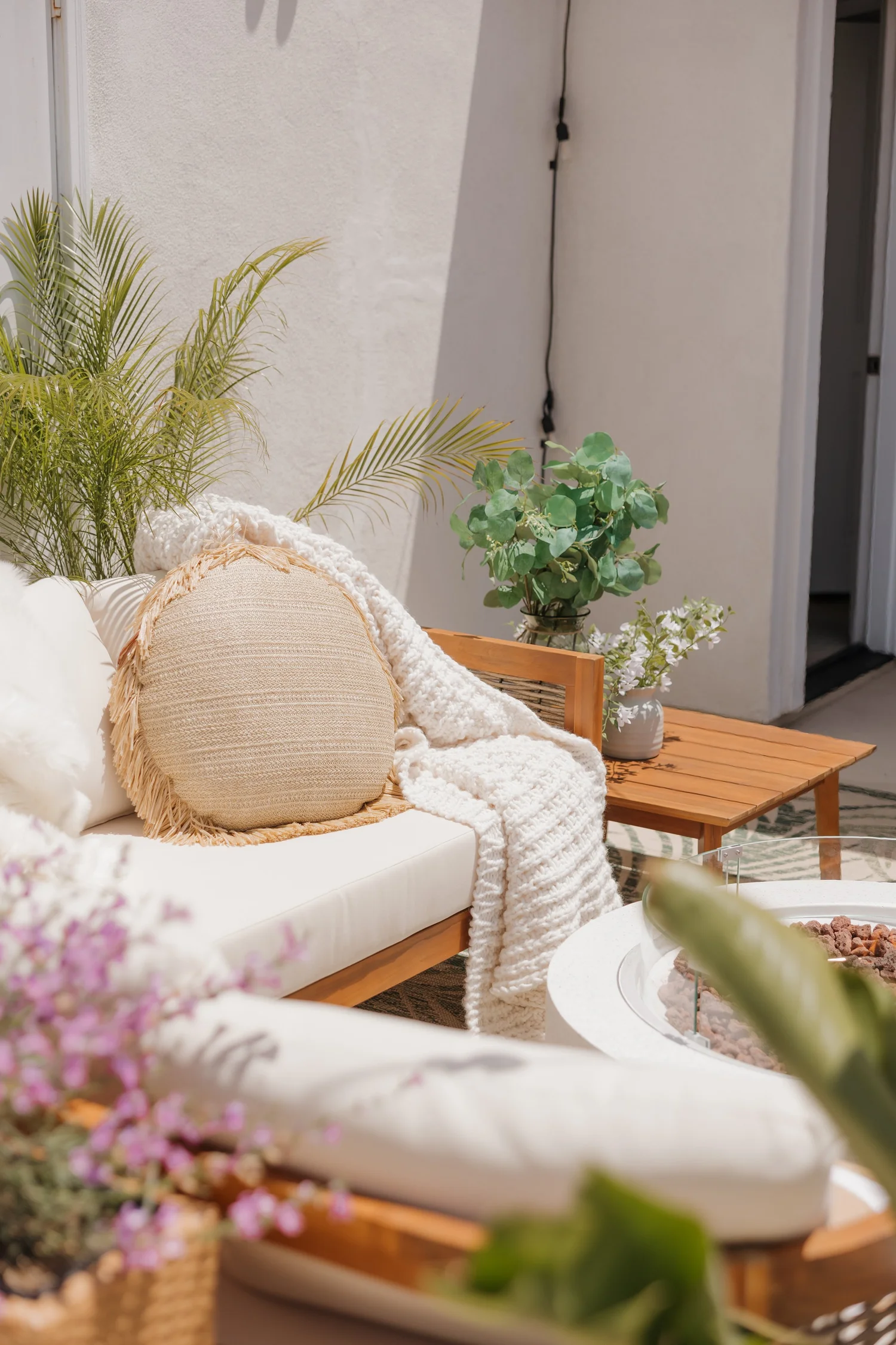 Outdoor sofa with woven pillows beside the fire table at Coastal Palm in Pacific Beach, designed by Salt and Sky Lodging Co.