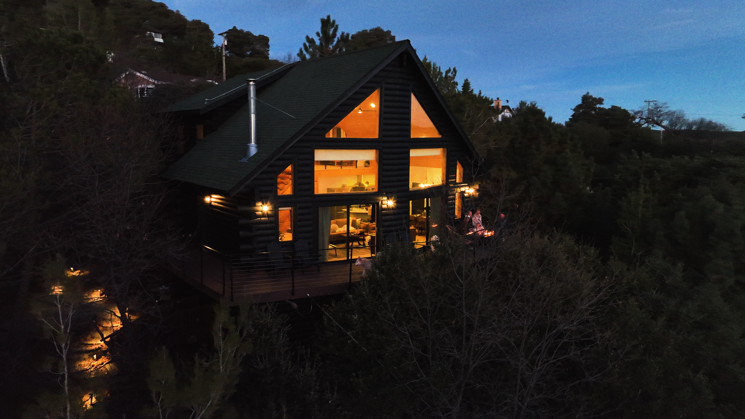 The A-frame lit up at dusk in the forest at Dark Moon Chalet in Julian, designed by Salt and Sky Lodging Co.