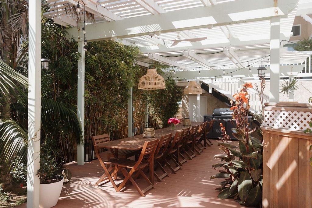 A long table under a pergola strung with lights, set for a group dinner