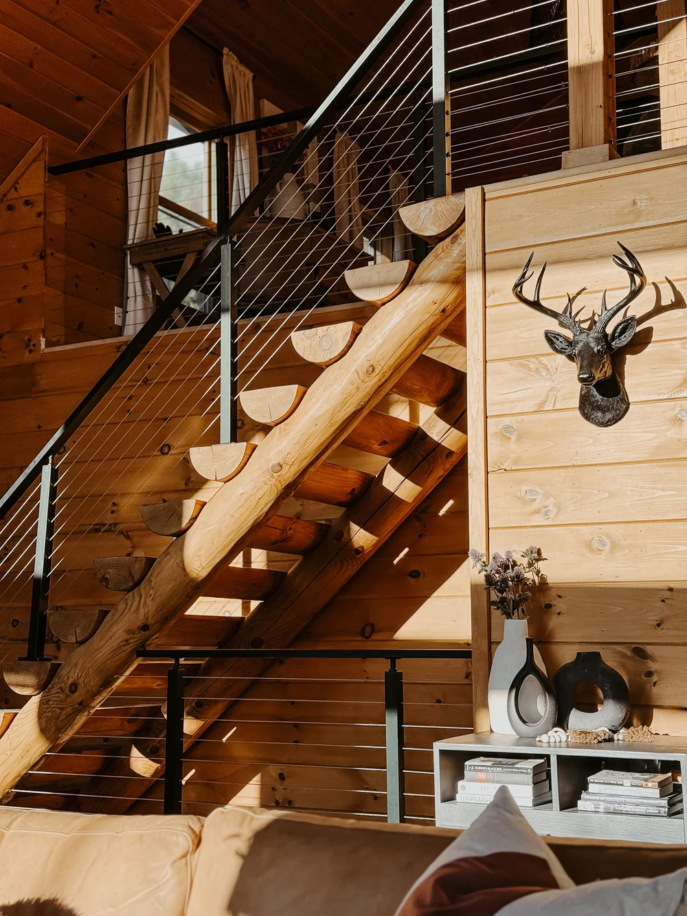 Log staircase with a cable railing and a deer mount at Dark Moon Chalet in Julian, designed by Salt and Sky Lodging Co.