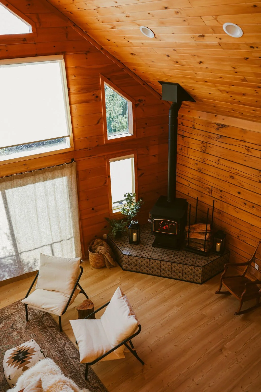 Corner wood stove with two lounge chairs under the tall A-frame windows at Dark Moon Chalet in Julian, designed by Salt and Sky Lodging Co.