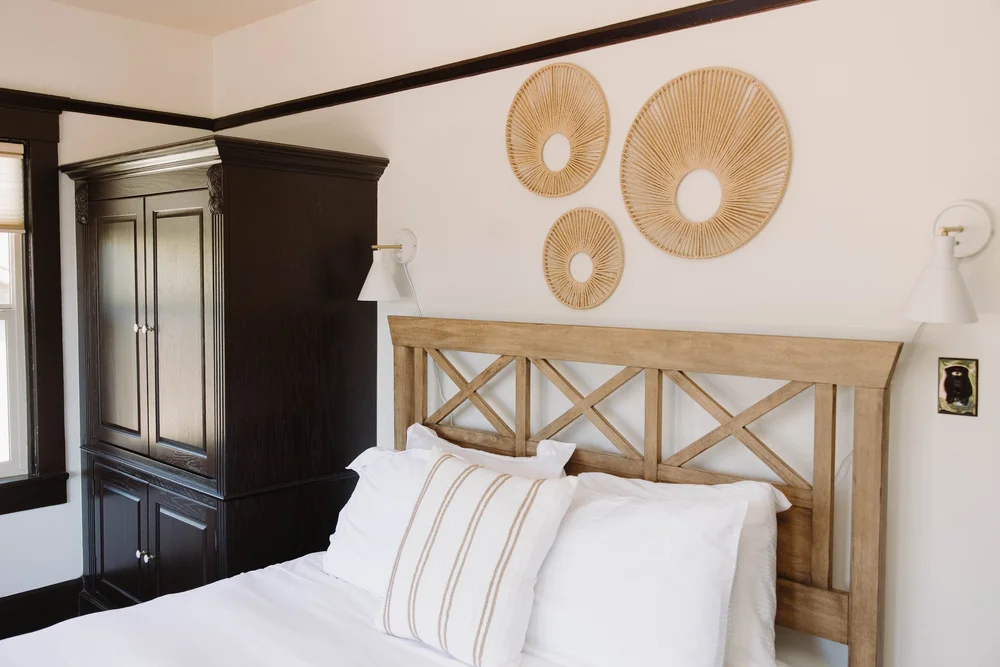 A queen bed with a wood headboard, woven wall baskets and a dark wood armoire in a second floor bedroom at Palm Parkside