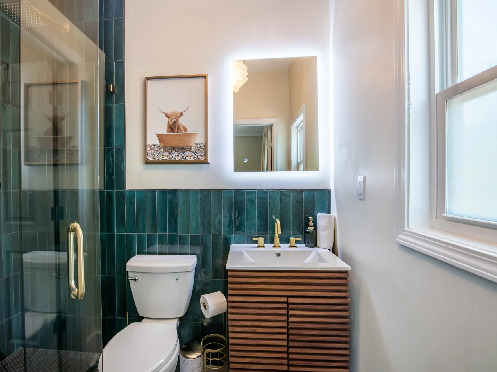 Bathroom with green tile, a lit mirror and a slatted wood vanity at Elmsgate in Birmingham, designed by Salt and Sky Lodging Co.