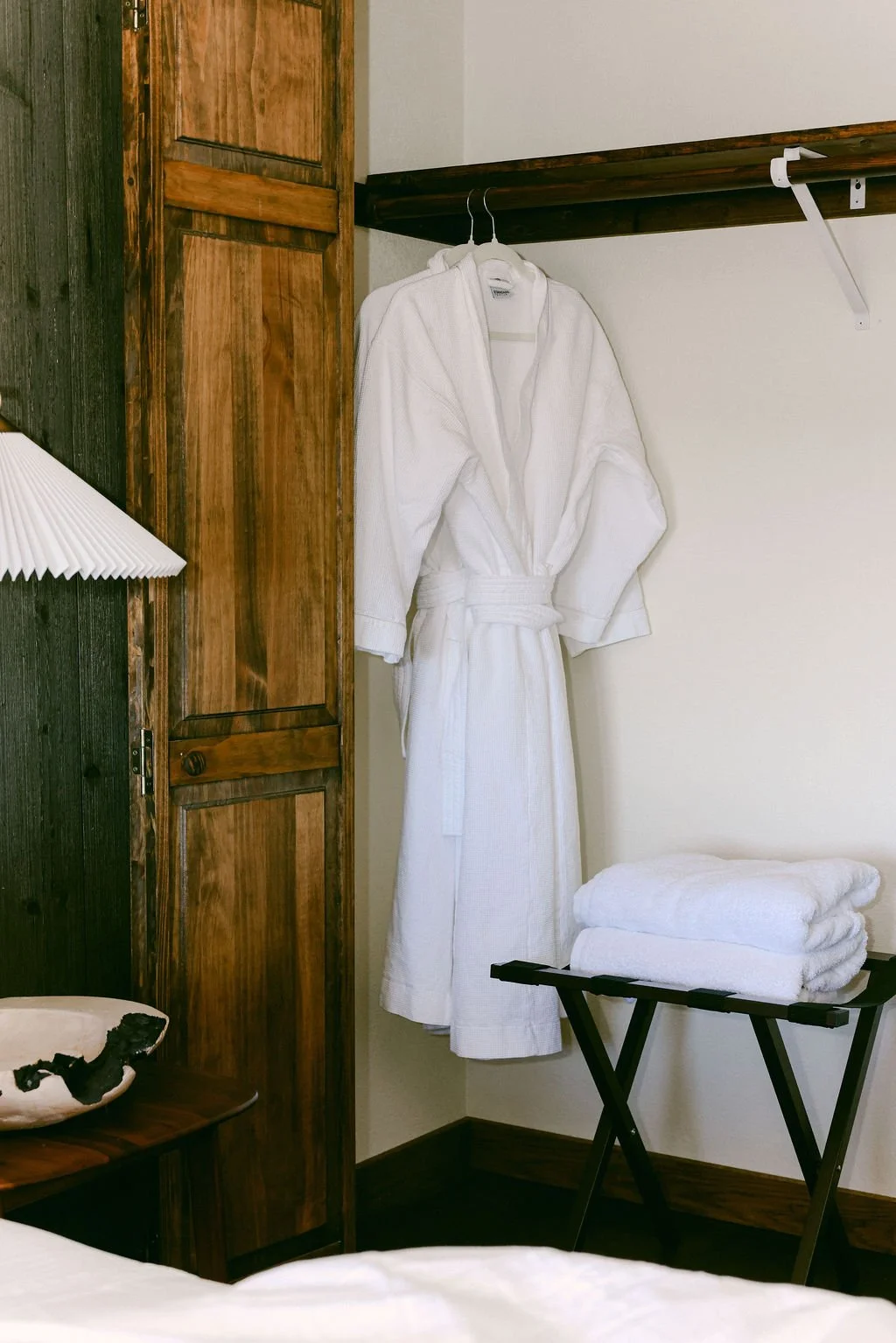 White bathrobe hanging on a wood rack beside folded towels