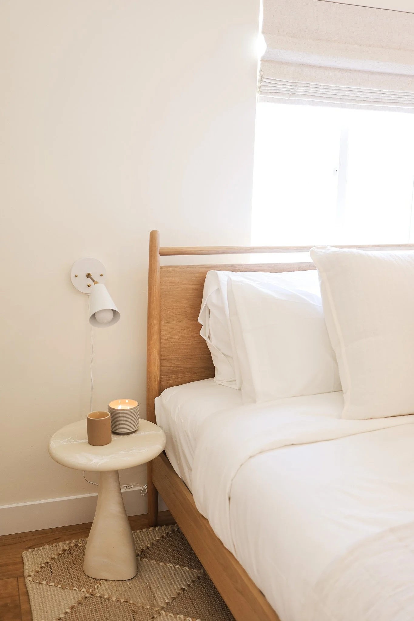 Bedroom with a wood headboard and a side table with a candle at Clementine C in Oceanside, designed by Salt and Sky Lodging Co.