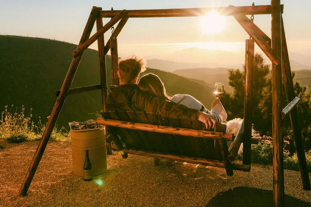 A couple on a wooden swing watching the sun set over the Julian mountains
