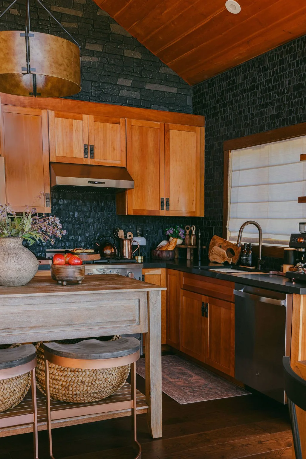 Cabin kitchen with wood cabinets, a dark tile backsplash and a vaulted wood ceiling