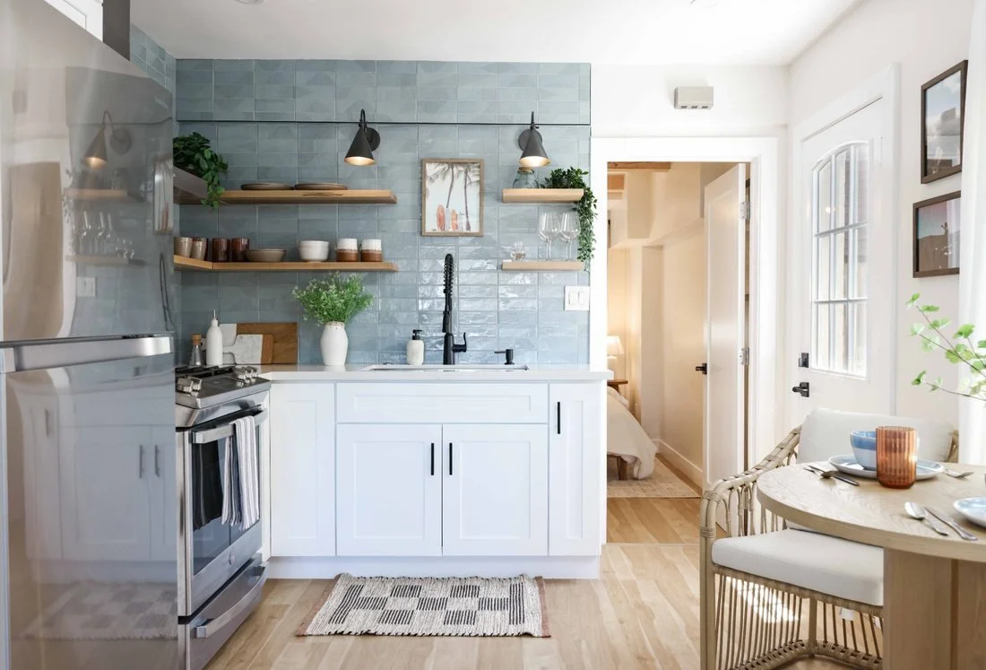 The kitchen at The Swell Unit Two in Oceanside, with a blue zellige tile backsplash, open shelving and a rattan dining set