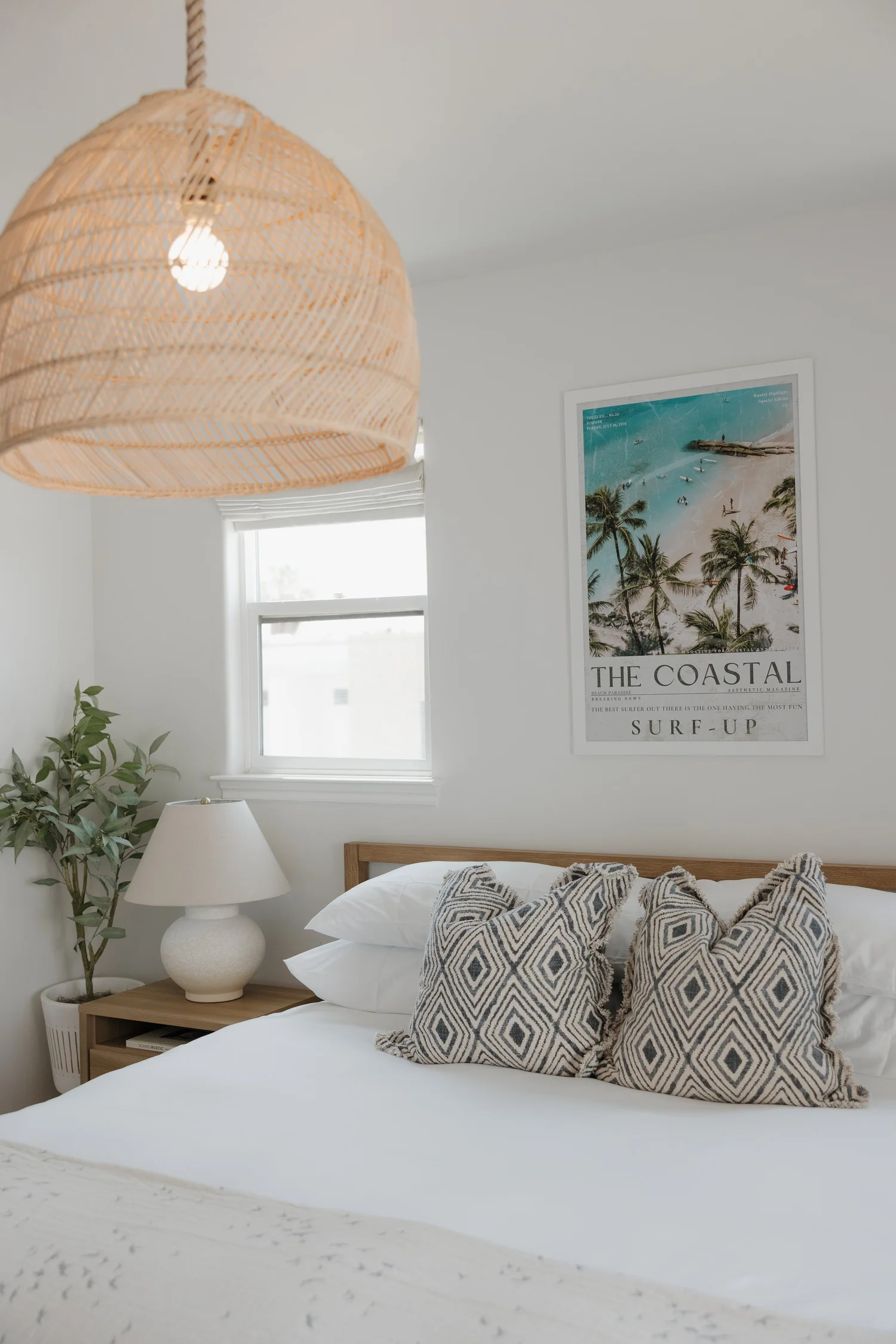 A bright bedroom at Coastal Palm in Pacific Beach, with a woven pendant light, white bedding and a vintage surf print
