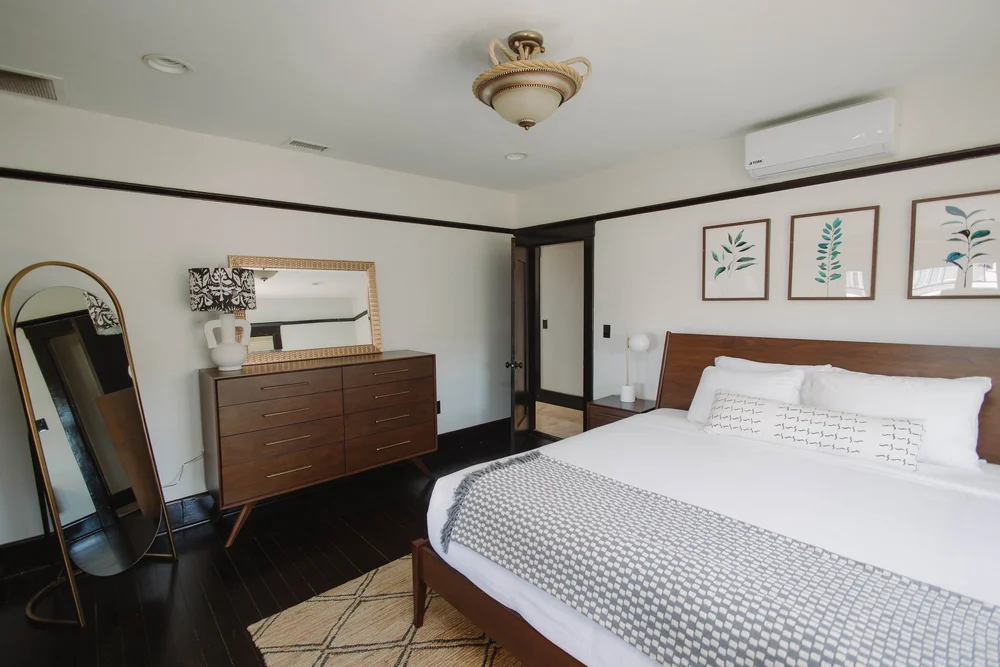 The king bed in the upstairs master suite at Palm Parkside, with a walnut dresser, an arched mirror and botanical prints