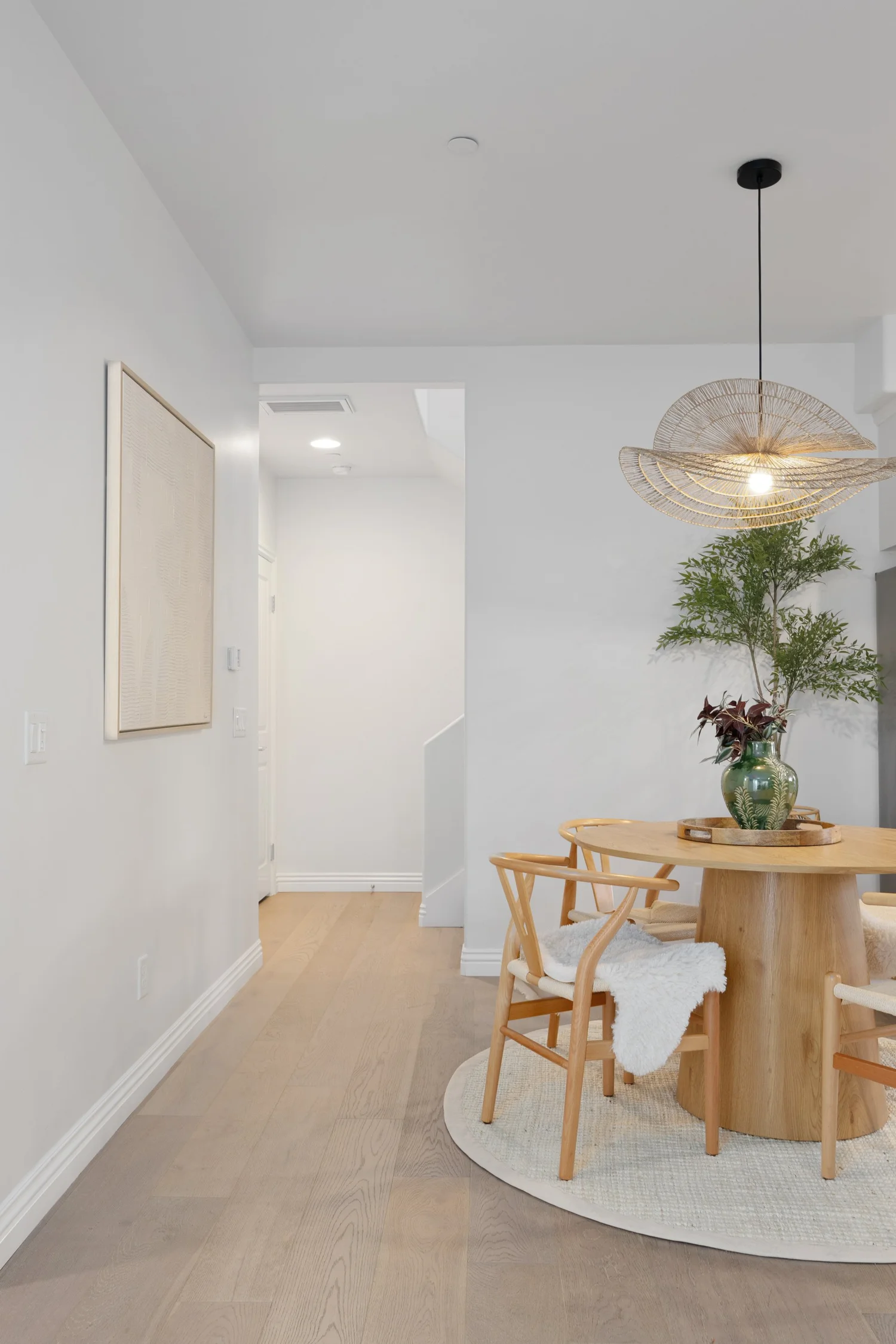 Dining nook with a round wood table, woven pendant and a palm at Coastal Palm in Pacific Beach, designed by Salt and Sky Lodging Co.