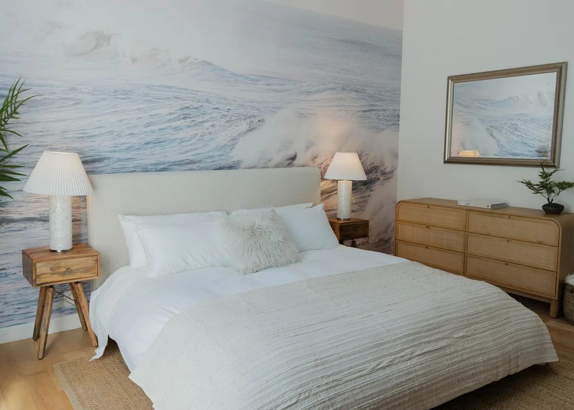 A bedroom at Velvet Surf in Pacific Beach with a wave mural behind the bed and cane furniture