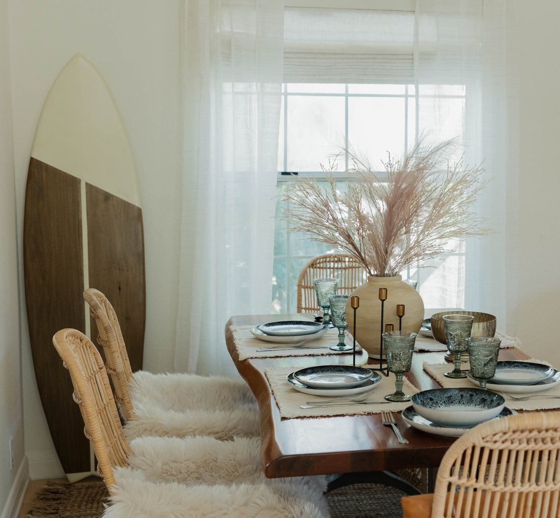 A dining room we designed, with a live edge table set for six, rattan chairs, sheepskin throws and a surfboard against the wall