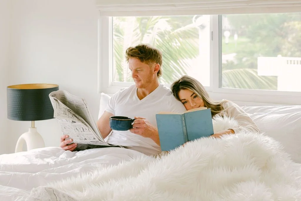 A couple reading the paper in bed with coffee in a bright coastal bedroom