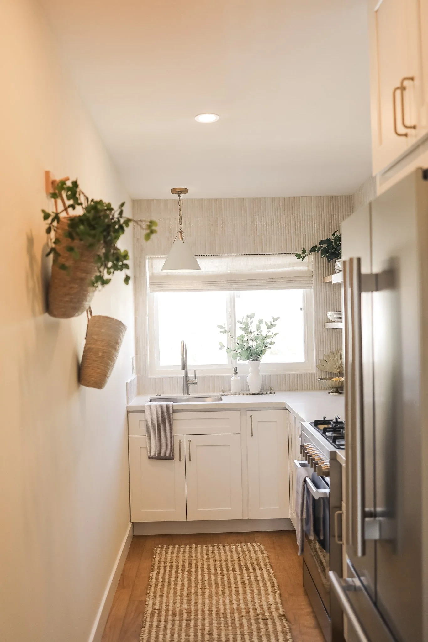 Galley kitchen with white cabinets and hanging baskets at Clementine C in Oceanside, designed by Salt and Sky Lodging Co.