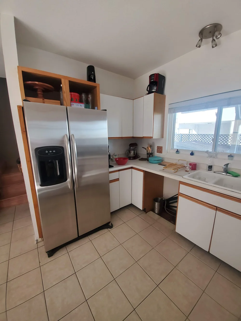 Before: Kitchen with white cabinets and a stainless fridge at OB Surfer's Paradise in Ocean Beach