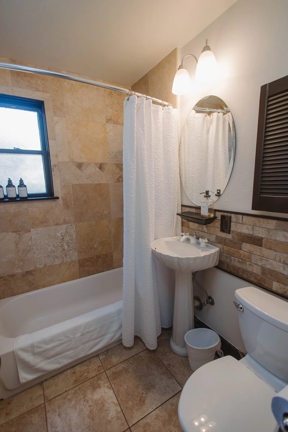 The first floor hall bathroom at Palm Parkside, with tan stone tile, a shell pedestal sink and a tub with a white shower curtain