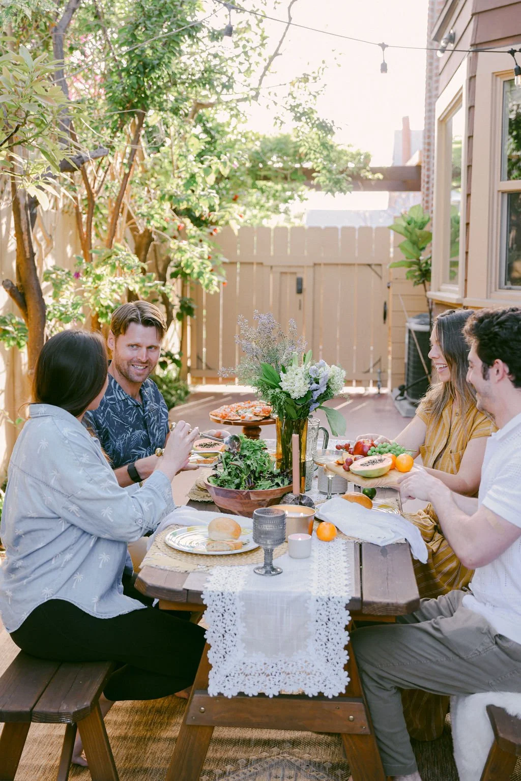 Family and friends sharing a meal at the picnic table under the string lights in the backyard at Palm Parkside