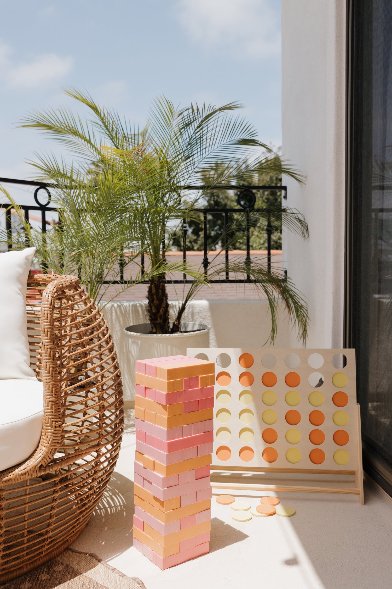 Balcony with a wicker egg chair, giant tumbling blocks and a palm at Coastal Palm in Pacific Beach, designed by Salt and Sky Lodging Co.